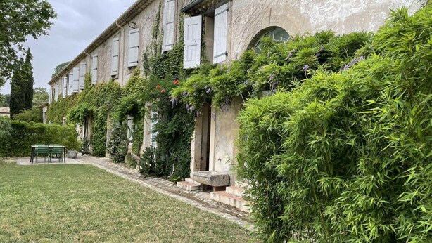 Ein traditionelles Gebäude mit Garten, darunter eine Rasenfläche, ein Tisch mit Stühlen sowie verschiedene Pflanzen und Sträucher.