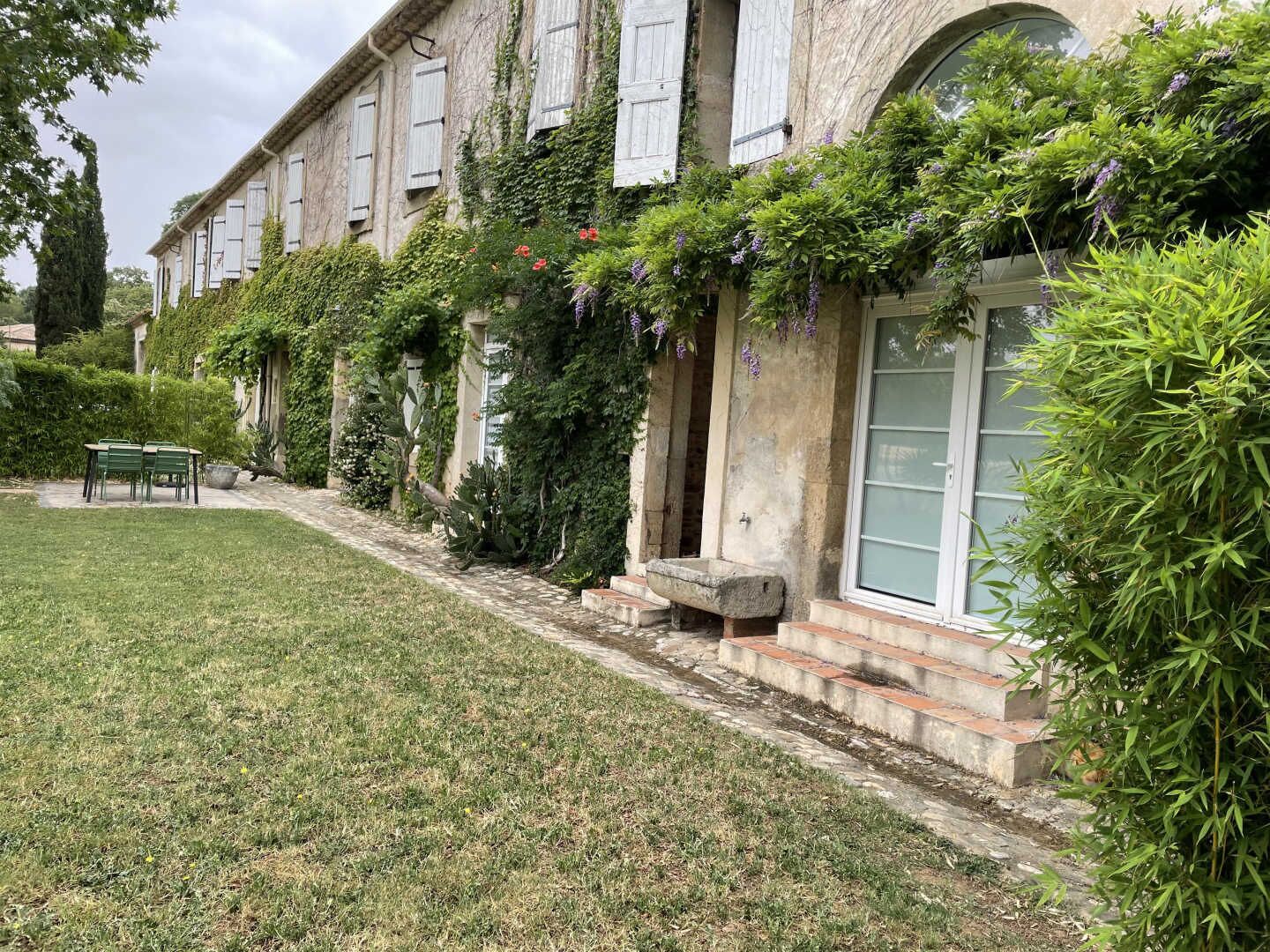 A historic building with a stone facade, white shutters, and a well-maintained garden with a lawn and a table with chairs.