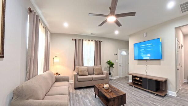 Ein modernes Wohnzimmer mit Ecksofa, Couchtisch, Fernseher und Deckenventilator.