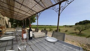 Ein Essbereich im Freien mit einem Holztisch, gedeckt für vier Personen, umgeben von Stühlen und einem darüberliegenden Pergola.
