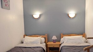Habitación doble con dos camas individuales, cabeceros de madera y mesitas de noche con lámparas.