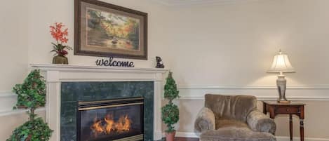 A living room with a fireplace, a sofa, a lamp, and a welcome sign above the fireplace.