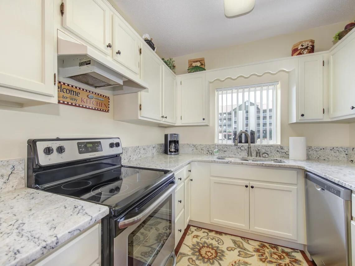 A kitchen with white cabinets, a stove, a coffee maker, and a window with blinds.