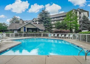 A swimming pool with a white fence, a small building with a porch, and a multi-story building in the background. - Two bedroom two bath condo| Pigeon Forge| Sleeps 4-6| City View (Pigeon Forge)