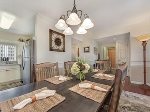 Comedor con una mesa de madera oscura dispuesta para seis personas, rodeada de sillas de madera. Un candelabro cuelga del techo, y un centro de mesa floral adorna la mesa.