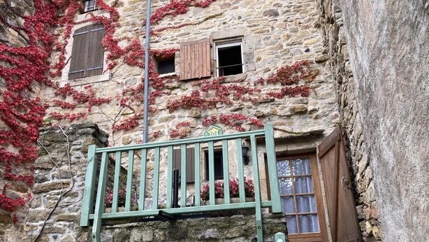 Un bâtiment en pierre aux murs recouverts de lierre, doté d’un balcon en bois et d’une petite fenêtre avec des volets.