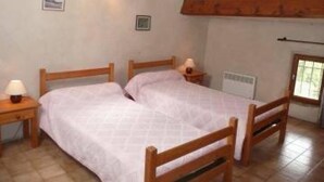 Une chambre avec deux lits en bois, une table de chevet avec une lampe, un radiateur fixé au mur et une fenêtre donnant sur un paysage verdoyant.