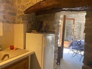 A rustic kitchen with a stone wall, a white refrigerator, and a small table with a chair.