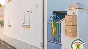 Un edificio blanco con entrada porticada, buzón y un pequeño cartel.