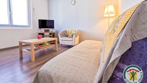 Habitación de hotel con cama, televisión, mesa, silla, lámpara y ventana.