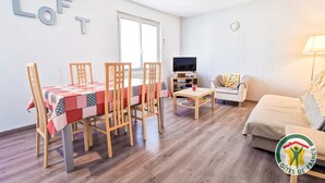 Una sala de estar con una mesa de comedor, sillas, un sofá, un televisor y una lámpara.