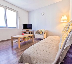 Une chambre d’hôtel avec un lit, une télévision, une table, une chaise, une lampe et une fenêtre.