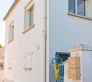 Un bâtiment blanc avec une entrée fermée par un portail, une boîte aux lettres et un petit panneau.