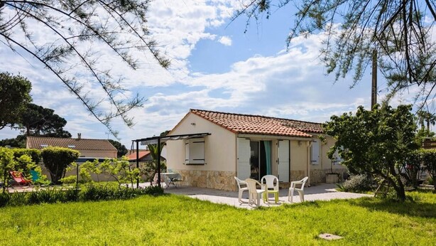 Una casa de una planta con techo de tejas, un patio con mobiliario exterior y un césped bien cuidado.