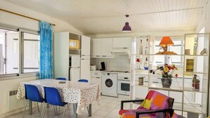 Cocina compacta con lavadora, una mesa de comedor con sillas y una silla colorida.