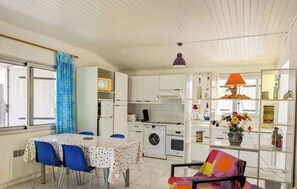 A compact kitchen with a washing machine, a dining table with chairs, and a colorful chair. - Villa Joseph - AGDE - Gîte (AGDE)