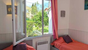 Un dormitorio con dos camas, una ventana con cortinas, un radiador y vistas a zonas verdes.