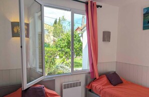A bedroom with two beds, a window with curtains, a radiator, and a view of greenery outside. - Villa Joseph - AGDE - Gîte (AGDE)
