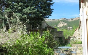 An outdoor patio with a table and chairs, surrounded by greenery and a mountain view.