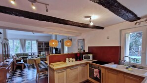 Eine kompakte Küche mit Holzausstattung, einer Mikrowelle und einem Spülbecken. Es gibt eine Essecke mit kariertem Boden und einem Sofa.
