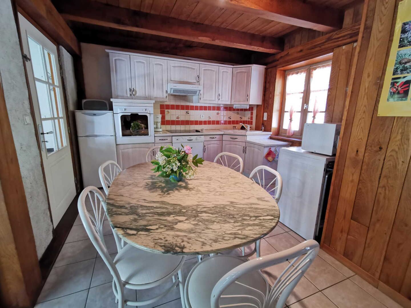 Une cuisine de taille réduite avec des meubles blancs, une table à manger en marbre et des chaises blanches.