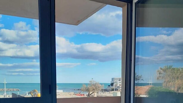 A balcony with a table and chairs, overlooking a beach and ocean.