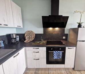 A compact kitchen with a black range hood, a built-in oven, and a white refrigerator.