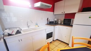 A compact kitchen with white cabinets, a sink, a stove, a microwave, and a refrigerator.