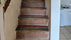 A wooden staircase with a handrail, leading to a room with a red wall and a white tiled floor.