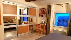Ein Schlafzimmer mit einem Bett, einem Schreibtisch, einem Stuhl, einer Kommode und einem Fenster mit Blick.