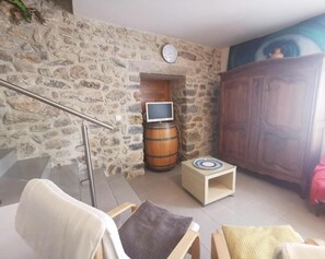 A room with a stone wall, a wooden cabinet, a television, and a small table with a clock. - Bergerie du Pic Saint-Loup (SAINT-ANDRE-DE-BUEGES)