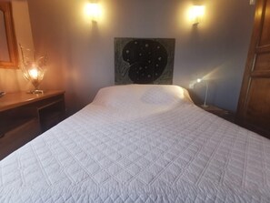 A bed with a quilted white cover, a wall-mounted clock, and two wall sconces.