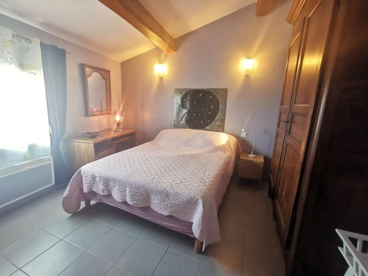 Une chambre à coucher comprenant un lit, des tables de chevet, une commode, un miroir et une œuvre d’art accrochée au mur.