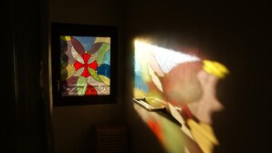 Ein Zimmer mit einem Buntglasfenster, einem kleinen Holzschemel und einem Fensterbrett.