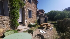 A stone building with a patio area featuring a table and chairs, a wooden bench, and a small garden with plants.
