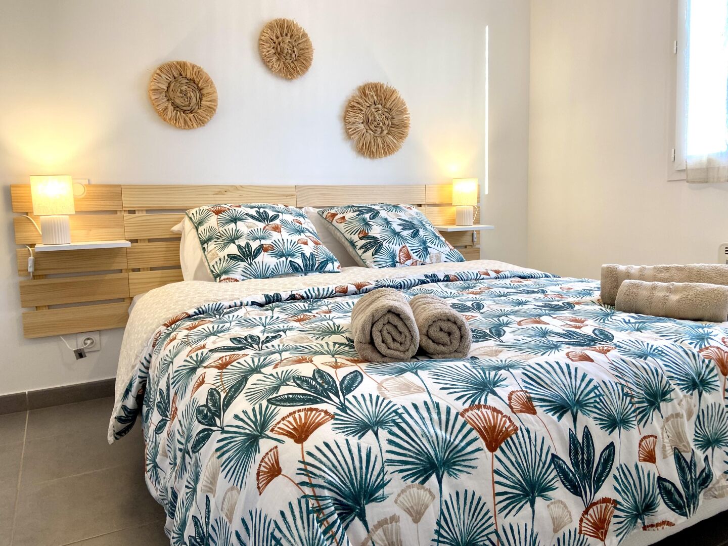 A hotel room with a bed, two bedside lamps, a headboard, and a wall with three wall art pieces.
