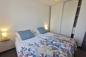A bedroom with two beds, each with a pillow and a bedside lamp. There is a wardrobe with a mirror and a hanging shelf.