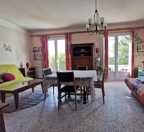A cozy living room with a dining table, chairs, a sofa, and a colorful rug.