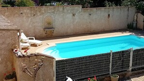 Ein Schwimmbecken mit gefliestem Sonnendeck, umgeben von einer niedrigen Mauer und Topfpflanzen.