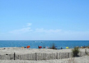 Ein sandiger Strand mit einem Holzzaun im Vordergrund und blauem, wolkenlosem Himmel.