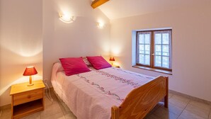 A bedroom with a wooden bed, two bedside lamps, a window with lace curtains, and a sloped ceiling. - La Bergerie - DIO-ET-VALQUIERES (DIO-ET-VALQUIERES)