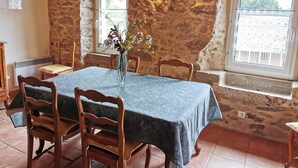 A dining area with a stone wall, a table with a blue tablecloth, wooden chairs, and a vase with flowers.