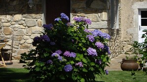 A stone building with a garden featuring hydrangea bushes.