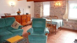 A cozy room with a wooden ceiling, a stone wall, a dining area with a table and chairs, and a sofa with a cushion.