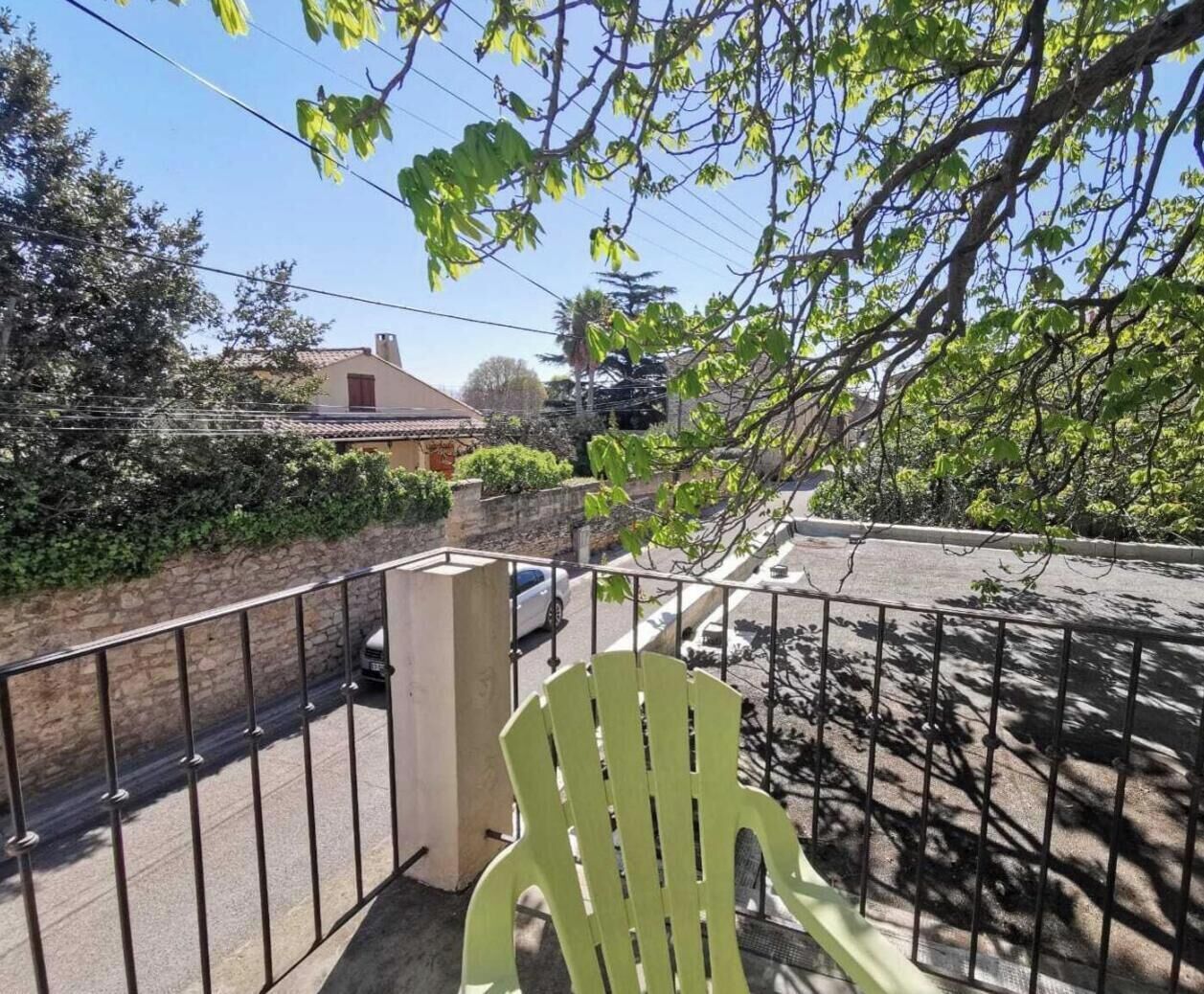 A balcony with a view of a street, a parked car, and a green chair.