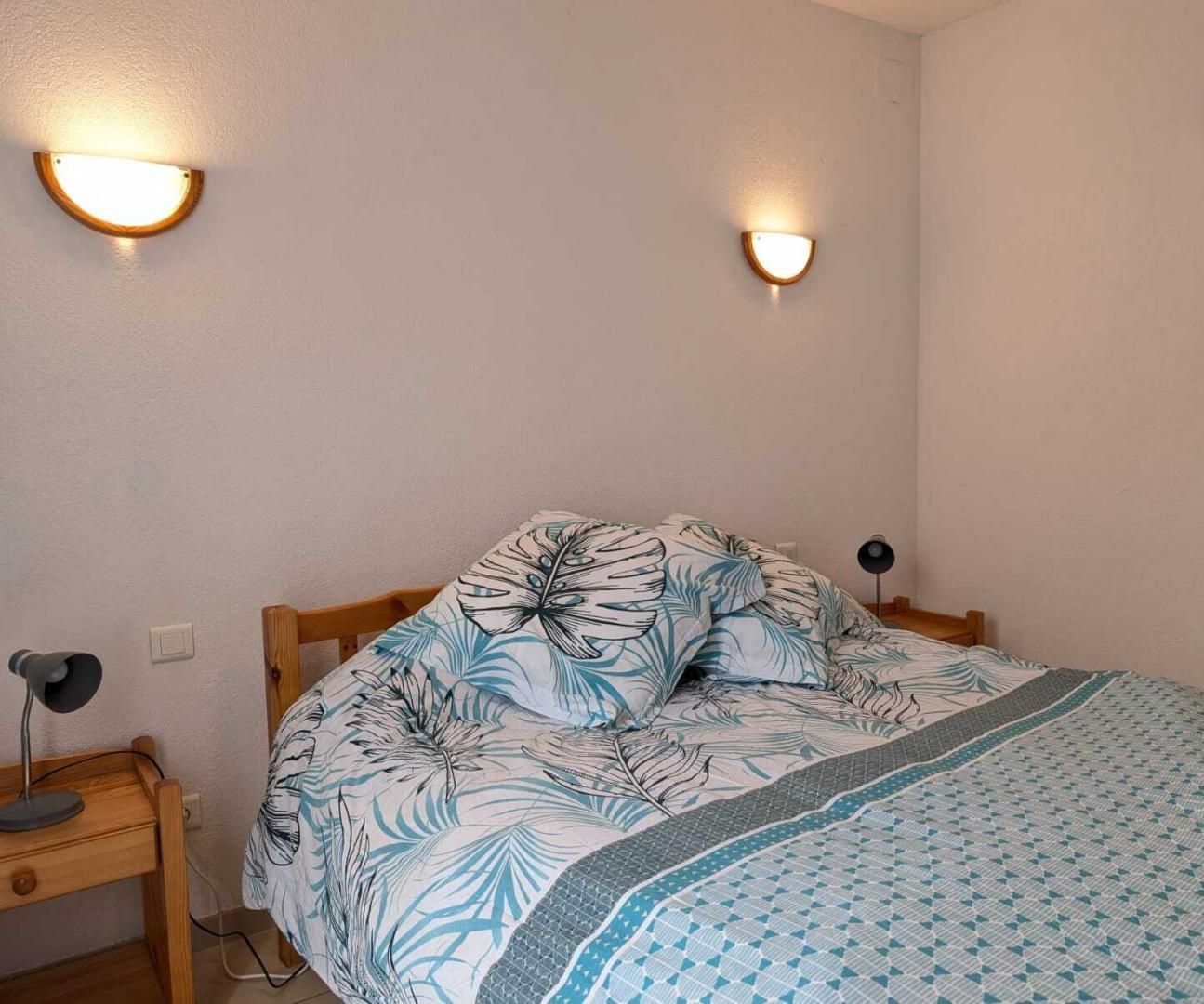 Un dormitorio con una cama, dos lámparas de pared, una mesita de noche y un cuadro en la pared.