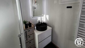 Ein kleines Badezimmer mit einem weißen Waschtisch, einer schwarzen Spüle, einem Spiegel und einer kleinen Pflanze.