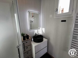 Une petite salle de bain avec un meuble-lavabo blanc, un évier noir, un miroir et une petite plante.