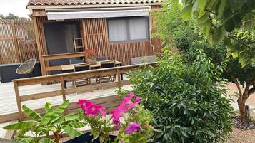 Een houten terras met tuinmeubilair, een overdekte zithoek en diverse planten.