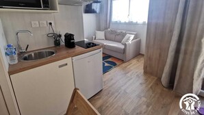 Eine kompakte Küche mit Mikrowelle, Spüle und Geschirrspüler. Im Wohnbereich befindet sich eine Couch und ein Fenster mit Vorhängen.